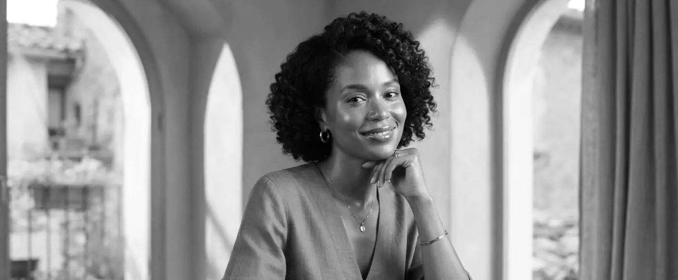 A woman smiling at a table under warm arched windows