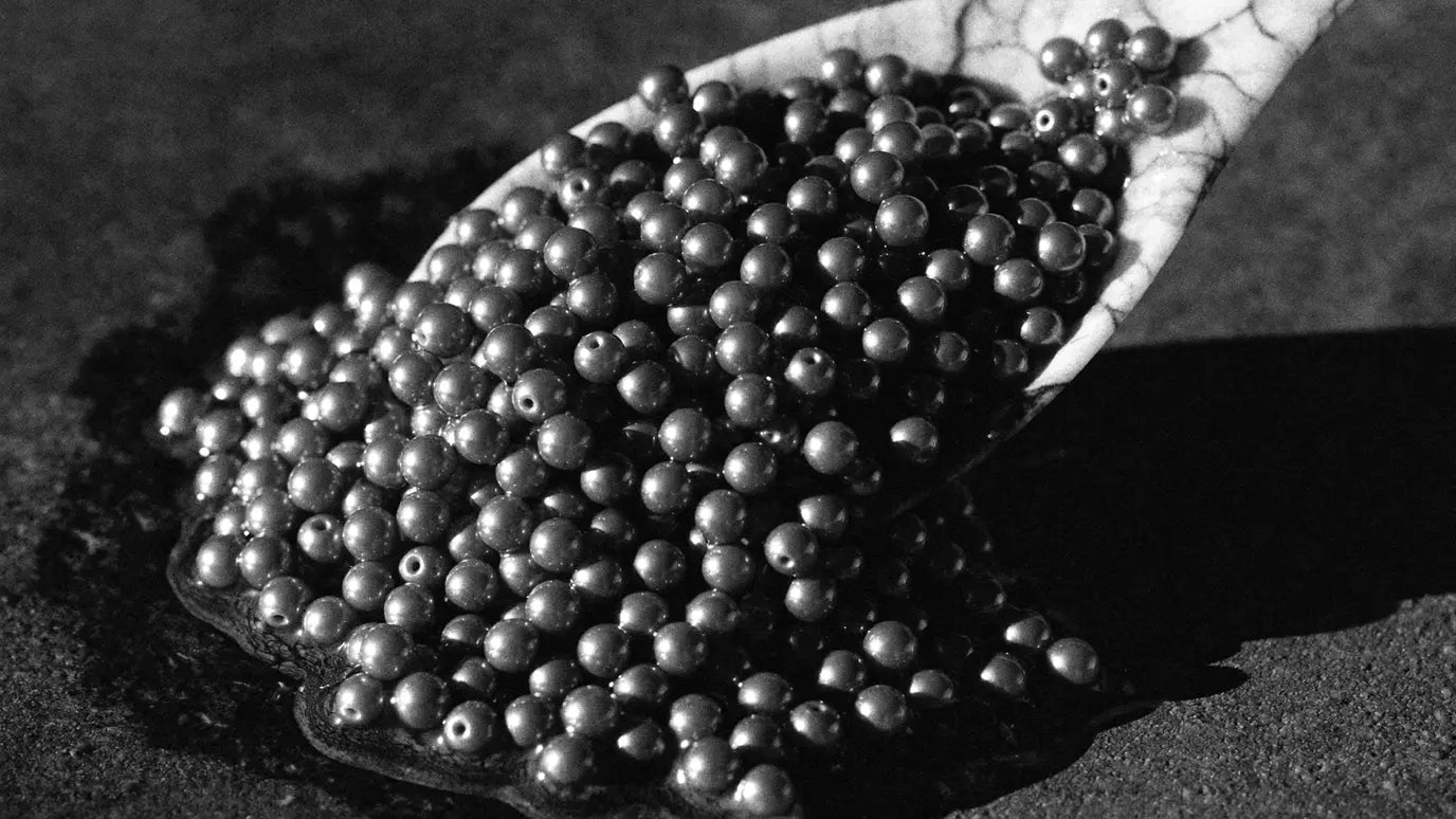 Caviar pearls spilling from a mother-of-pearl spoon onto dark stone