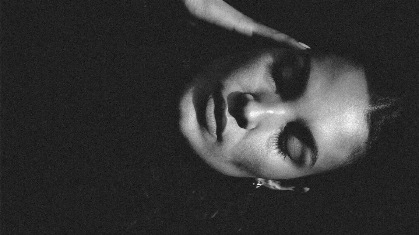 Close portrait of a woman in soft side light, eyes closed, fingertips at her temple