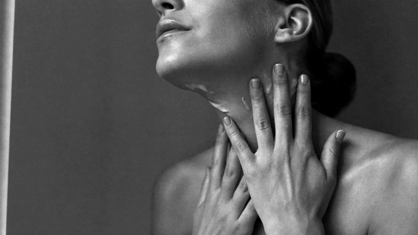 Hands smoothing serum upward along the jaw in soft window light